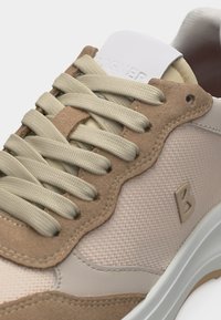 Baskets beiges et fauves avec des lacets épais en tissu, garniture en daim, panneau latéral en mesh et logo "B" embossé sur le côté extérieur.