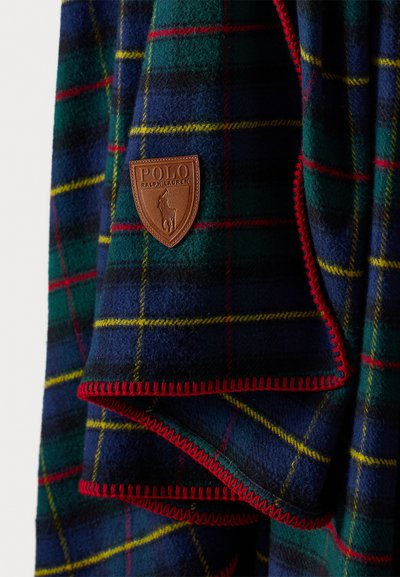 Flisasti karirani pokrivač u tamnoplavoj, zelenoj i žutoj boji s crvenim rubom. Sadrži kožnu oznaku Polo Ralph Lauren na jednom rubu.