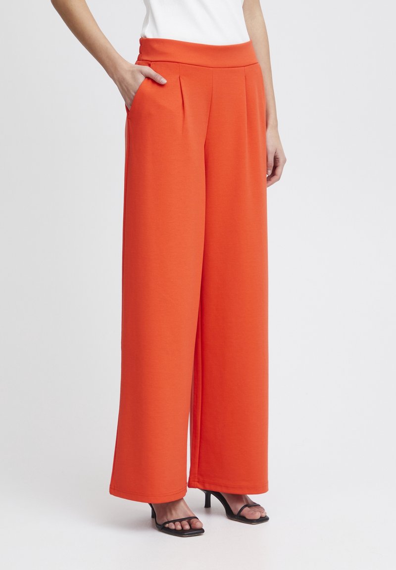 Orange vida byxor med hög midja, med sidfickor och veck för extra detaljer. Bärs med svarta öppna klackar.