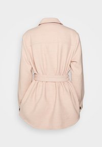 Chaqueta rosa claro con cintura ceñida, cuello con solapa, mangas largas y un corte holgado, fabricada en un tejido texturizado y con detalles de botones.