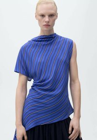 Top a righe blu e bianche con un design asimmetrico, caratterizzato da drappeggi sul davanti, maniche corte e una texture liscia.