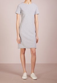 Robe grise à rayures avec des manches courtes, un col rond et longueur genou. Associée à des baskets blanches. Texture de tissu lisse. Détails de design minimalistes.