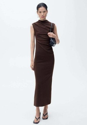 Robe midi sans manches, couleur marron, avec un col montant et des détails drapés, associée à un sac à main noir et des sandales plates. Texture lisse.