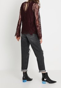 Bordeaux blonde top med dyb V-udskæring på ryggen, parret med slidte sorte jeans og blanke sorte ankelstøvler med blå blokhæle.