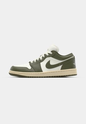 Baskets Nike basse en cuir vert olive et blanc. Les caractéristiques incluent une semelle en caoutchouc, un système de laçage et un logo swoosh bien en évidence sur le côté.
