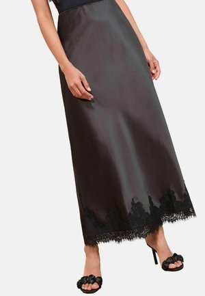 Schwarzer Satinkilt mit Spitzenbesatz am Saum, der eine glatte Oberfläche und ein fließendes Design aufweist. Getragen mit schwarzen Absatzsandalen.