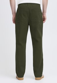 Zöld, elasztikus derékpántú nadrág két nagy hátsó zsebbel, egyenes szárú kialakítással és sima textúrával. Lábbeli világosbarna szandál.