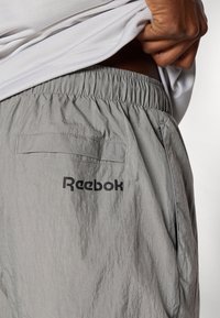 Svetlo sivé šortky Reebok s elastickým pásom, bočnými vreckami a zadným vreckom, s čierne vytlačeným logom. Textúrovaná tkanina.