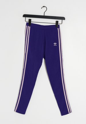 Leggings violets Adidas avec des bandes latérales rose clair suspendus à un cintre noir sur fond blanc.
