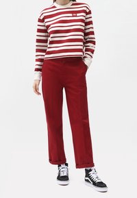 Červeno-bíle pruhovaný dlouhý rukáv top, zkombinovaný s červenými kalhotami s vysokým pasem a černými vysokými teniskami. Jednoduchý design s volným střih.