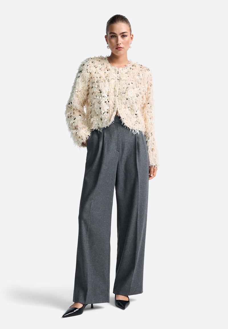 Cream-colored, fluffy textured cropped cardigan with sequins, paired with gray wide-leg trousers and pointed black heels.