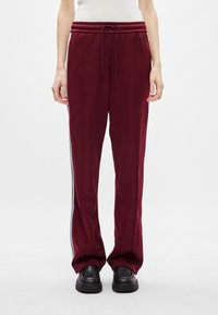 Μπλούζες σε μπορντό χρώμα, κατασκευασμένες από μαλακό ύφασμα, διαθέτουν μέση με κορδόνι, λευκές πλαϊνές ρίγες και άνετη εφαρμογή, συνδυάζονται με μαύρα παπούτσια.