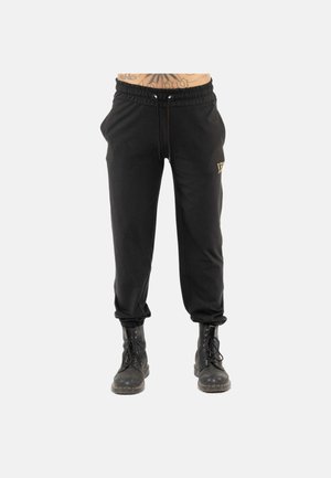 Pantaloni jogger neri con vita elasticizzata e coulisse indossati con stivali da combattimento neri con lacci su sfondo semplice.