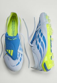 Chaussures à crampons bleues et blanches avec semelles et accents jaune néon, lacets blancs lâches, et languettes bleues affichant le texte "EST 1994".