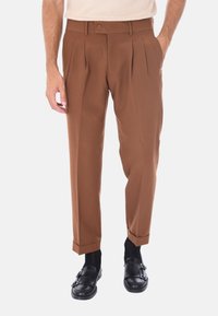 Pantaloni marroni a pieghe con una vestibilità su misura, realizzati in tessuto liscio. Presentano una chiusura con bottone, orli con risvolto e sono abbinati a scarpe nere senza lacci.