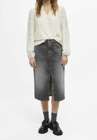 Weiße, strukturierte Bluse mit langen Ärmeln und V-Ausschnitt, kombiniert mit einem grauen Jeansrock mit Schlitz vorne und schwarzen Plateauschuhen.