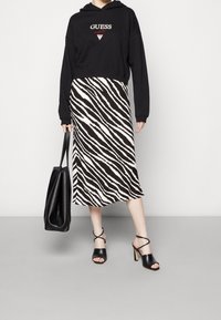 Svart croppad hoodie med röd broderad logotyp, tillsammans med en midi kjol i svart och vitt zebra mönster. Svarta öppna klacksandaler och väska.