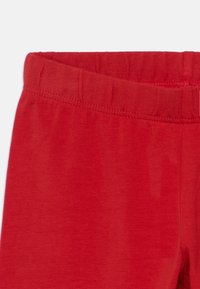 Czerwone legginsy o miękkiej fakturze, z elastycznym paskiem w talii i gładkim wykończeniem. Materiał ma jednolity kolor, bez wzorów czy akcentów.