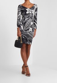 Svart och vit blommig klänning med trekvartslånga ärmar och V-ringning, i kombination med en texturerad svart handväska och svarta sandaler med remmar.