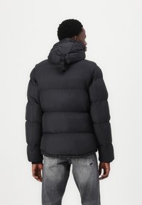 Black puffer jacket with a hood, featuring a cinched collar and adjustable clasp. The material appears smooth and insulated, with a puffy design.