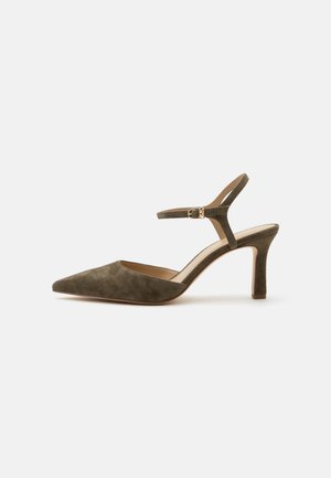 Zapato de tacón medio de ante verde oliva con puntera puntiaguda y correa ajustable en el tobillo con pequeña hebilla dorada sobre fondo blanco.
