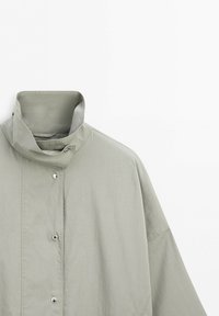 Light gray high-collar jacket with snap button closure, displayed against a neutral background.