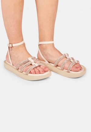 Sandales rose clair avec une semelle texturée, dotées de plusieurs brides scintillantes et d'une boucle à la cheville. Matériau lisse avec une base plate et amortissante.