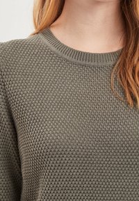 Grå texturerad tröja med rund halsringning och ribbad kant. Har ett våffelmönster och mjukt tyg.