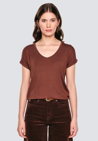 Brązowa, krótkorękawowa koszulka V-neck wykonana z miękkiego materiału, zestawiona z ciemnobrązowymi sztruksowymi spodniami. Prosty design z podwiniętymi mankietami rękawów.