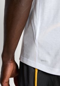 Camisa atlética blanca con costuras planas y etiqueta "DRYCELL" en el costado, combinada con pantalones cortos negros que tienen una franja amarilla.