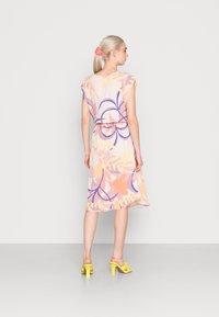 Vestido floral em tons pastel com mangas curtas, cintura ajustada, bainha com babados e textura leve. Combinado com mules de salto amarelas.