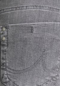 Tissu en denim gris avec une poche arrière ornée de rivets en argent et de détails de couture. La texture semble lisse avec un tissage en denim visible.