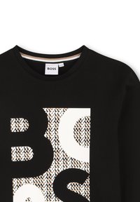 T-shirt noire avec un grand logo "BOSS" blanc doté d'un motif texturé en marron et crème, col rond et manches courtes.