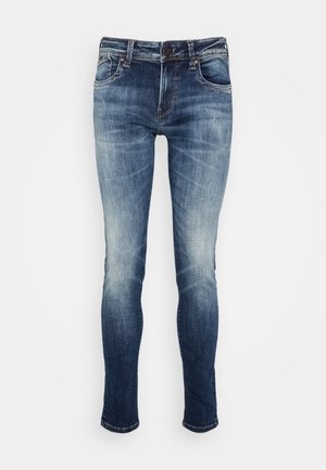 Jean en denim bleu avec une coupe slim, présentant un délavage, des poches standard et une fermeture éclair avec un bouton. Texture lisse et sans motifs.