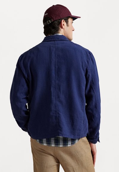 Navy blue linen jacket with a casual design, standard collar, and straight cut, worn over a checkered shirt; textured fabric visible.