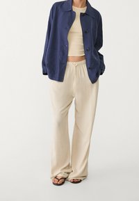 Marineblauw jasje met knopen, lichtbeige broek met elastische taille, en zwarte teenslippers. Soepele texturen, casual pasvorm, eenvoudig ontwerp.
