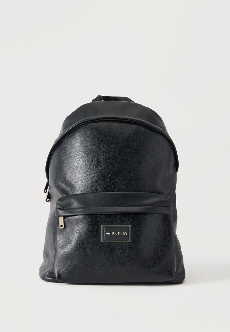 Sac à dos noir en simili cuir avec poche zippée sur le devant et étiquette VALENTINO, design simple sur fond uni clair.