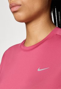 T-shirt de sport ajusté rose avec un col rond et le logo Nike argenté sur la gauche de la poitrine. Texture de tissu lisse et extensible.