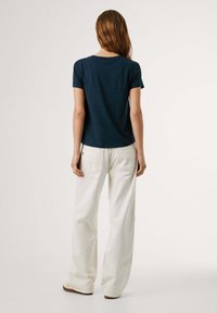 T-shirt blu navy a maniche corte con scollatura rotonda, abbinato a pantaloni bianchi a gamba larga, dotati di tasche posteriori e dal taglio morbido.