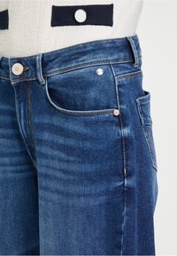 Blauwe denim jeans met een klassieke snit. Kenmerken zijn een metalen knoopsluiting, zijzakken en subtiele vervaging langs de benen.