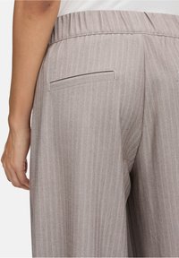 Lichtbruine, herringbone-patroon broeken met een vlakke tailleband en een enkele achterzak. Zachte textuur zichtbaar, sluit nauw aan bij de taille.