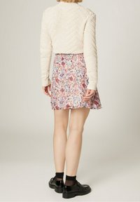 Suéter grueso de punto en color crema con cuello de canalé, combinado con una falda mini de estampado floral en tonos rosa, azul y crema, y zapatos de plataforma negros.
