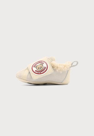 Kremfarvet småbørnsko med blød foer, velcrobånd med et tøjdyr-logo og ordet "Moschino," samt en stofløkke ved hælen.