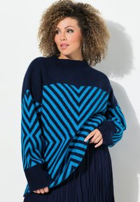 Un pull bleu et marine à motif, présentant un design en chevrons avec un col rond et des poignets côtelés, associé à une jupe noire plissée.