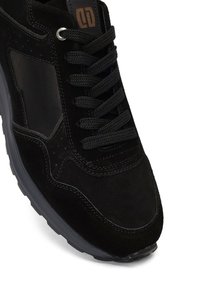 Sneaker in suede nero con accenti testurizzati, lacci tondi e colletto imbottito. Presenta una suola in gomma nera a contrasto e dettagli perforati.