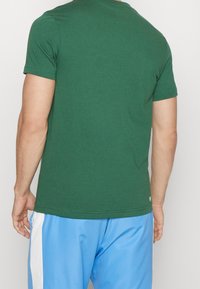 Vihreä puuvillainen t-paita pyöreällä pääntiellä ja lyhyillä hihoilla, yhdistetty vaaleansinisiin shortseihin, joissa on valkoiset sivukoristeet.