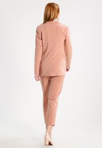 Světle růžový oblek s dobře padnoucím blejzrem a zúženými kalhotami. Jemná textilie, minimalistický design a jeden roz vent na zadní straně. Jasné akcenty na obuvi.