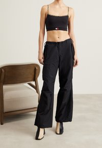 Pantaloni cargo neri con vestibilità ampia e cordoncino regolabile. Abbinati a un top nero con spalline a stampa leopardata. Scarpe nere con tacco.