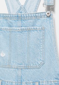 Hellblaue Denim-Latzhose mit großer Fronttasche, gekreuzten Trägern und Metallverschluss auf der rechten Seite.
