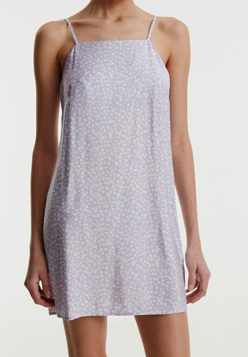 Liliowa sukienka na ramiączkach z cienkimi paskami, ozdobiona białym wzorem kwiatowym. Miękka, lekka tkanina o luźnym kroju i prostym dolnym wykończeniu.